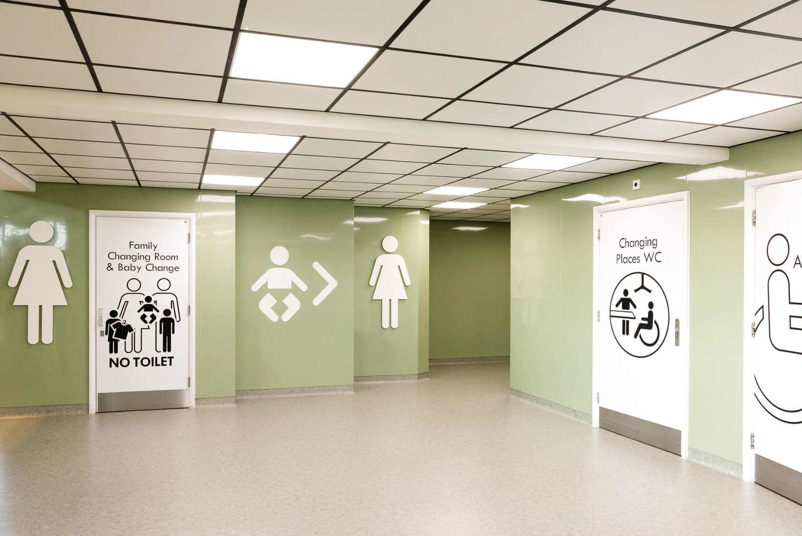 A clean, modern hallway with clear signage for a family changing room, baby changing area, accessible toilet, and Changing Places WC.
